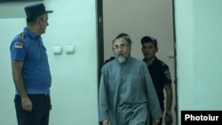 Archbishop Mikael Ajapahian being escorted to the courtroom at the start of his trial at a criminal court of general jurisdiction in Yerevan on August 15, 2025.