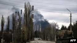 Ukraine - A military vehicle drives on a road as smoke rises from a power plant after shelling outside the town of Schastia, near the city of Lugansk, February 22, 2022.
