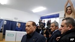 Сильвіо Берлусконі, лідер партії «Вперед, Італіє!» (ліворуч) прибуває на виборчу дільницю в Мілані аби проголосувати на парламентських виборах, а активістка руху Femen (справа на задньому плані) оголеним виглядом та написом на грудях нагадує 81-річному екс-прем’єрові, що він «засидівся» у політиці.