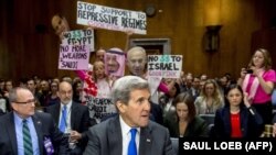 همزمان با حضور جان کری در نشست کمیته روابط خارجی سنا در اسفند ۹۴، معترضان پلاکاردهایی را در مخالفت با کمک‌های مالی و نظامی به عربستان، مصر و اسرائیل بر سر دست دارند.