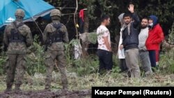 Polish border officers stand guard next to a group of migrants stranded at the frontier between Belarus and Poland earlier this month. 