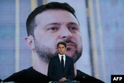 Прем’єр Франції Габріель Атталь стоїть перед екраном і зображенням президента України під час дебатів напередодні першого туру позачергових парламентських виборів. Париж, 27 червня 2024 року