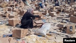 یک زن فلسطینی در حال جست‌وجو در کارتن‌های «بنیاد بشردوستانه غزه» (جی‌اچ‌اف)؛ رفح، پنجشنبه ۱۵ خرداد