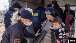 Makedoniýanyň polisiýa ofiseri bosgun zenany we çagany barlagdan geçirýär.