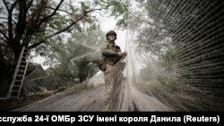 Військовослужбовець 24-ї механізованої бригади імені короля Данила Збройних сил України встановлює протидронові сітки над дорогою