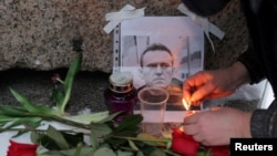 Людина запалює свічку біля портрета російського опозиціонера Олексія Навального біля пам’ятника жертвам політичних репресій, Санкт-Петербург, Росія, 16 лютого 2024 року