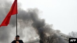 Участник антиправительственной демонстрации несет флаг Кыргызстана. На заднем плане – костры возле захваченного офиса президента страны. Бишкек, 7 апреля 2010 года. 