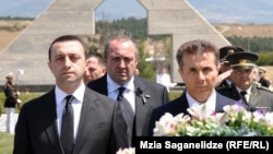 Кейбір сарапшылар Грузия премьері Ираклий Гарибашвили (сол жақта) мен президент Георгий Маргвелашвили (ортада) арасындағы кикілжіңге миллиардер Бидзина Иванишвилидің  (оң жақта) қатысы бар деп болжайды.  