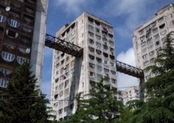 Багатоповерхові будинки в горбистому передмісті Тбілісі з «небесним мостом». Архітектурне рішення забезпечує швидке і просте переміщення між верхнім пагорбом і сусідніми районами, без виснажливого підйому або спуску по схилу. Люди можуть піднятися на ліфті, а потім пройти по мосту через розташований у висотці продуктовий магазин на вершину найближчого пагорба