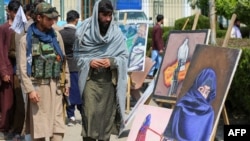 Taliban təhlükəsizlik əməkdaşları Cəlalabadda rəsm sərgisinin yanından keçərkən burkalı qadın portretinə baxırlar.