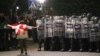 Протестираща с грузинското знаме се разхожда пред полицейски кордон в столицата Тбилиси, 4 октомври 2025 г.