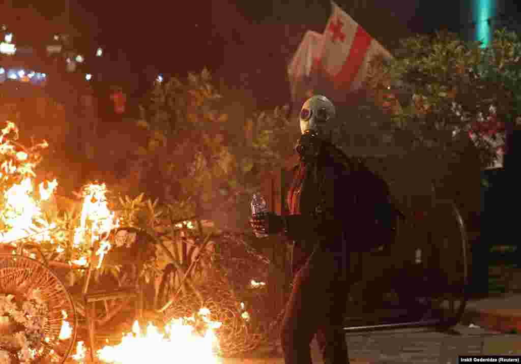 Опозиційні демонстрації розпочалися ще вдень, але ближче до ночі вони втратили мирний характер: демонстранти пішли на штурм палацу Орбеліані, поліція почала розгони, стала з'являтися інформація про постраждалих.На фото – протестувальник у протигазі на тлі палаючих барикад із меблів. Як повідомив кореспондент «Еха Кавказу» (проєкт Радіо Свобода), спецпризначенці застосовували сльозогінний газ