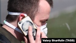 Чоловік у масці розмовляє по телефону, на чохлі якого зображений президент Росії Володимир Путін