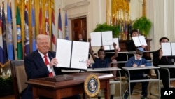 Прэзыдэнт Дональд Трамп трымае падпісаны выканаўчы ўказ, а маладыя людзі трымаюць копіі ўказу, падпісанага ім у Белым доме. Вашынгтон, 20 сакавіка 2025 году