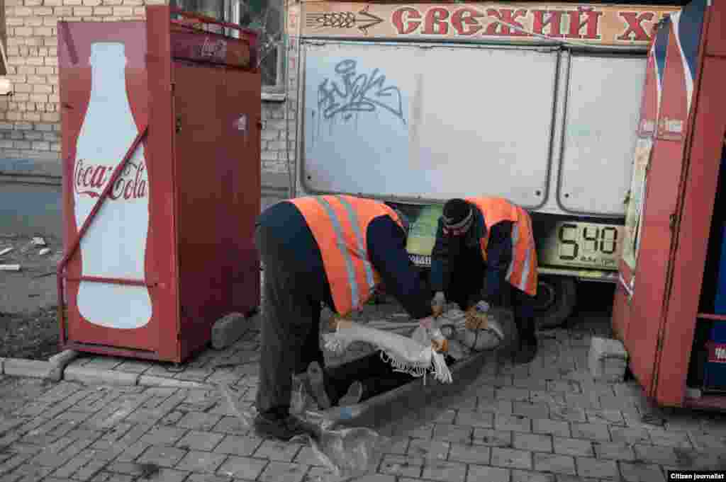 Donetsk, Ukrain. Several artillery shells hit the very city centre, which has never happened before. It is the last day befor ceasefire. Undertakers load a body of killed woman to a strecher.