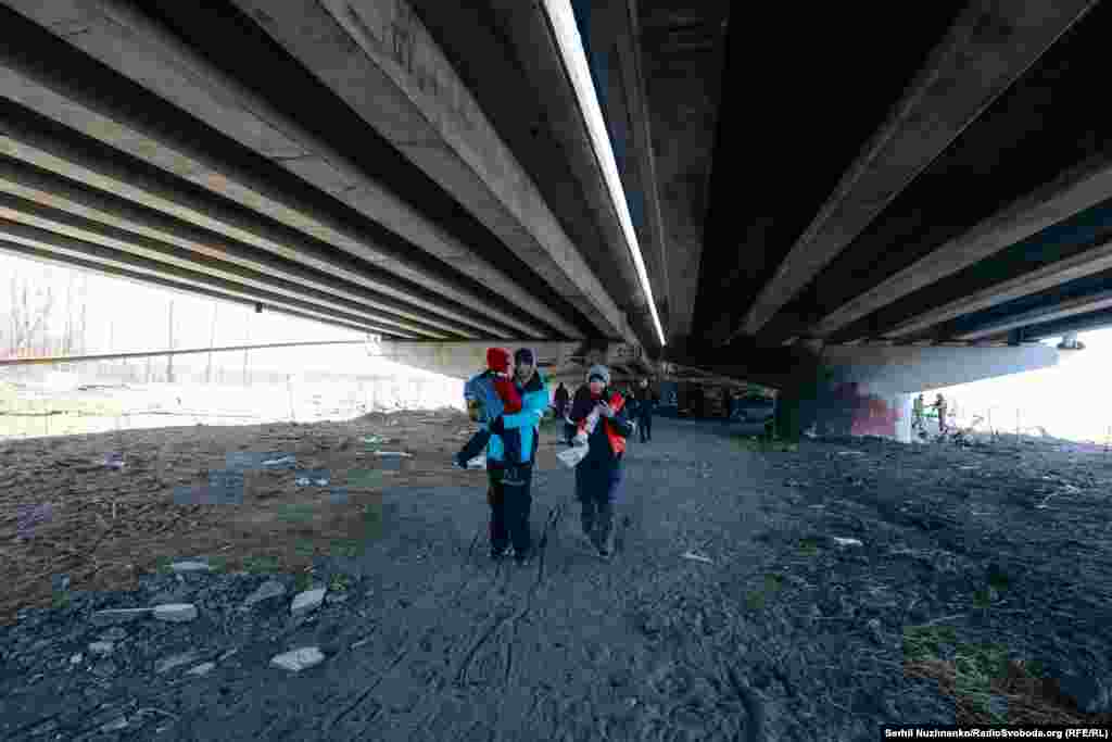 Сям’я зь дзецьмі хаваецца ад абстрэлаў пад апорамі ўзарванага Раманаўскага мосту.Зьлева фота 11 сакавіка 2022 году, справа — з сакавіка 2025 году