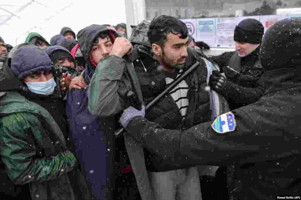 A policeman pushes migrants as they wait to be relocated at the Lipa camp on December 26. The camp was to be closed on December 23 and relocated. However, officials said the move had to be postponed since the camp was almost entirely destroyed in the fire. Bosnia has become a bottleneck for thousands of migrants hoping to reach neighboring European Union member Croatia and then head toward other Western EU members.