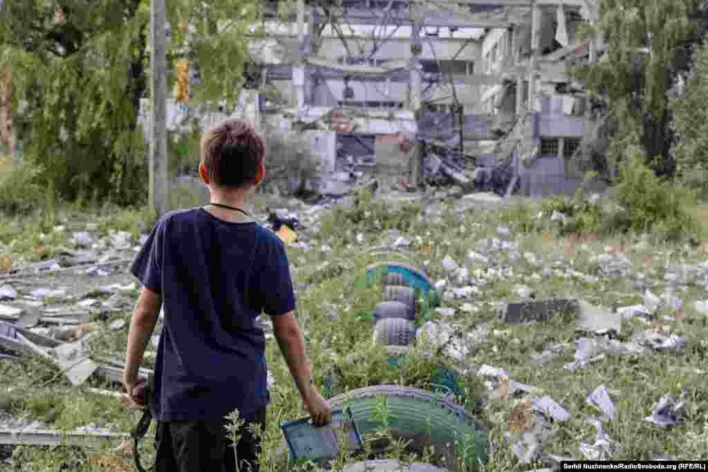 Хлопчык глядзіць на тое, што засталося ад ягонай школы, якую зруйнаваў авіяўдар расейскай арміі. Уся трава вакол засыпаная раскіданымі выбухам сшыткамі і кніжкамі. Бахмут, Данецкая вобласьць, чэрвень 2022 году. За час расейскай узброенай агрэсіі ва Ўкраіне цалкам зьнішчана больш за 400 школ, а кожная сёмая школа зазнала пашкоджаньні
